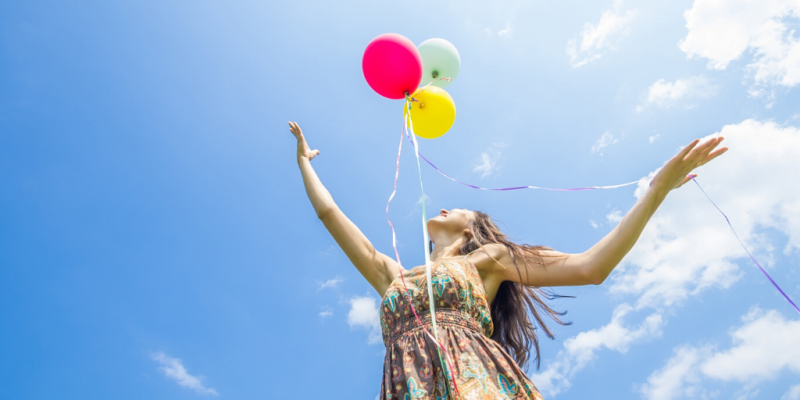 Woman releasing multicolored balloons into clear blue sky