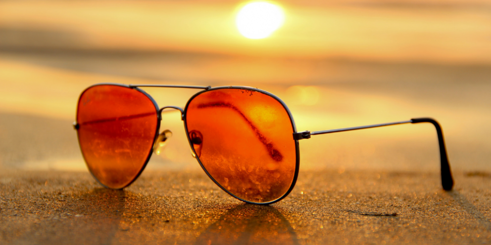 Orange sunglasses on the sand with sun shining behind them