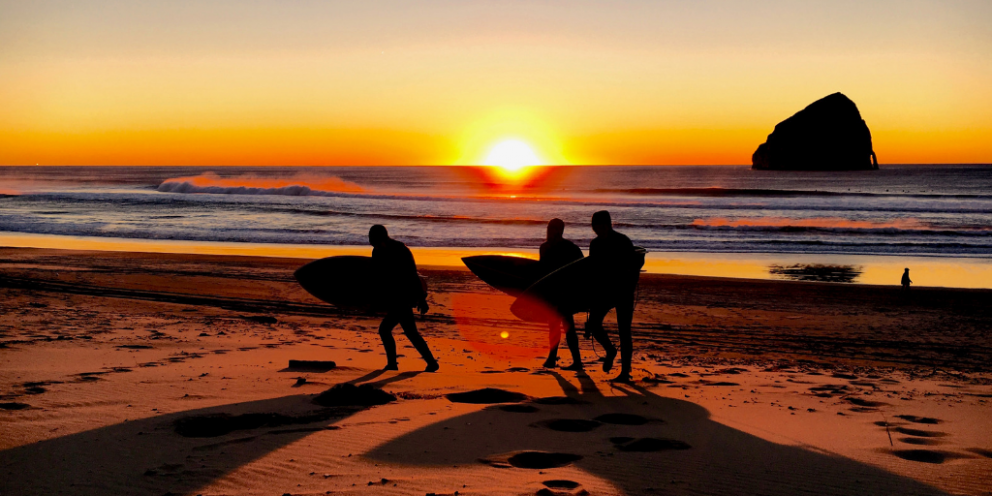 Three surfers leaving the beach at sunset