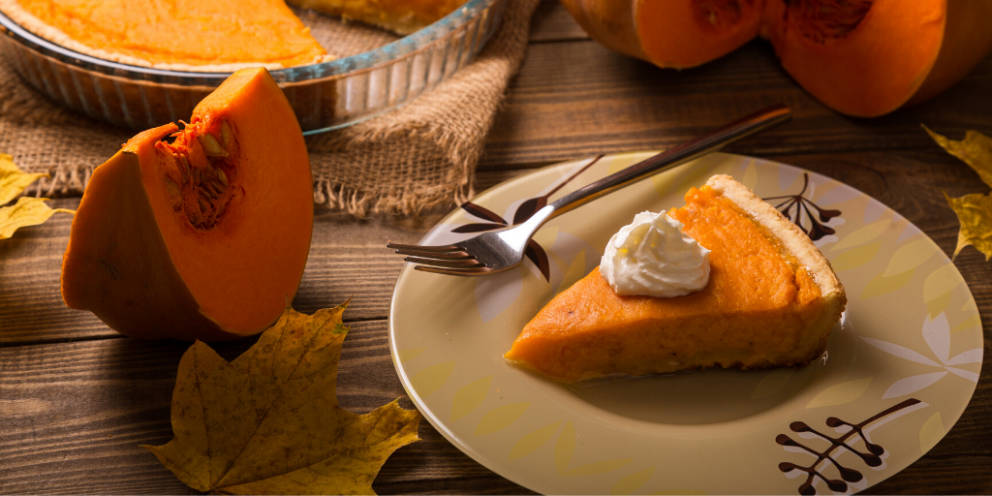 Slice of pumpkin pie with cream on plate and cut up pumpkin next to it