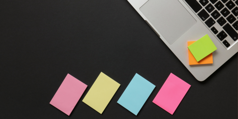 Four stacks of differently colored post-it notes next to open laptop with two more stacks of post-it notes on top of one another