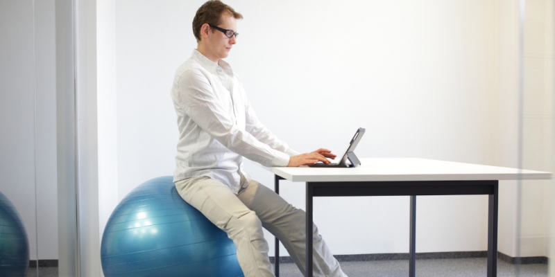 Developer sitting on a stability ball to counteract back pain from working on computer