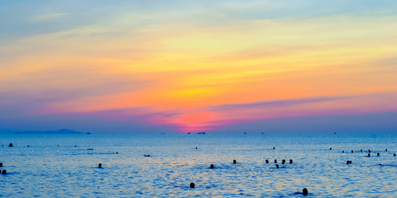 People swimming in the sea during sunset