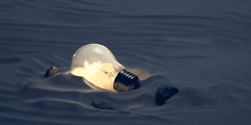Illuminated lightbulb lying in sand