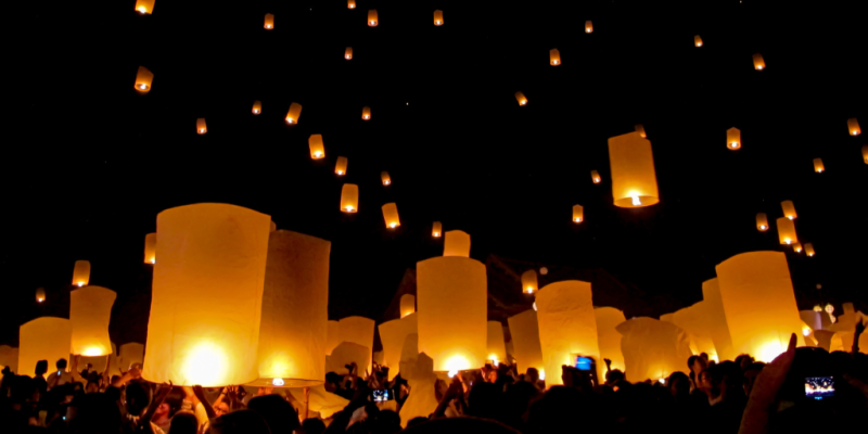 People releasing lit lanterns into the air at night as part of some kind of festival and/or tradition